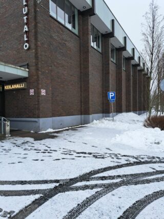 Korkea rakennus, jonka seinustalla pysäköintipaikkaa osoittava liikennemerkki.
