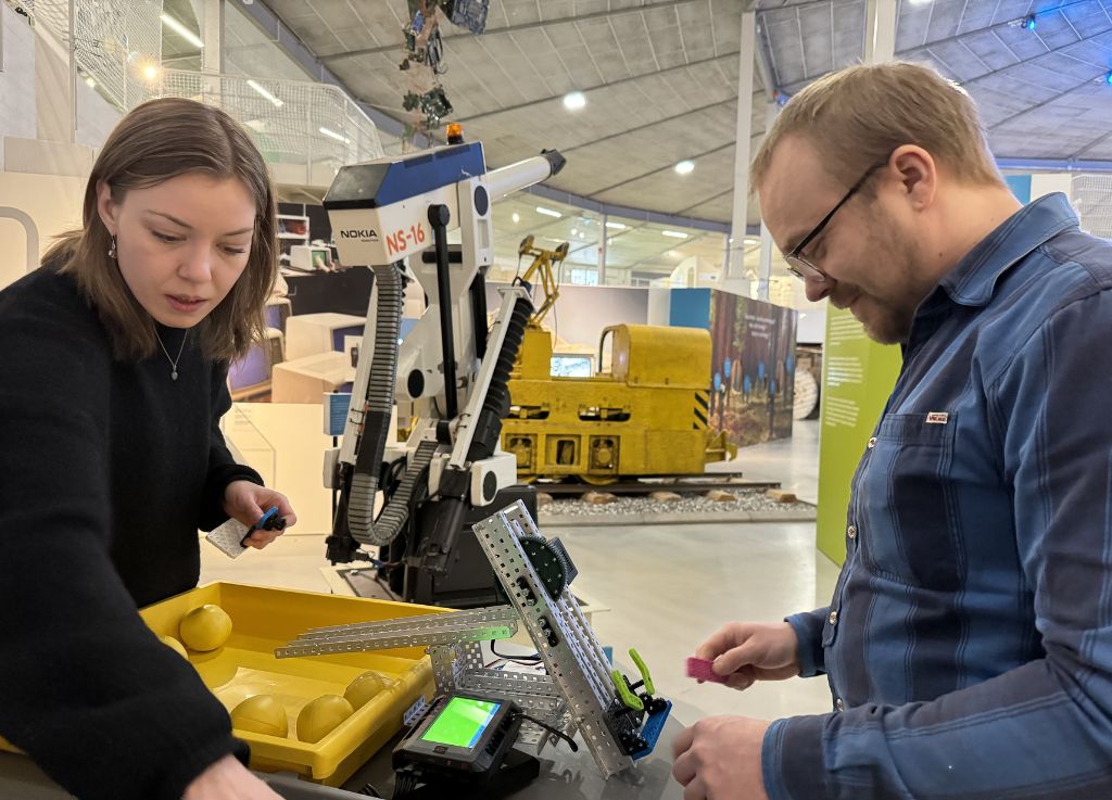 Kaksi nuorta aikuista rakentelemassa avarassa pyöreässä tilassa seisten jotakin robotin näköistä.