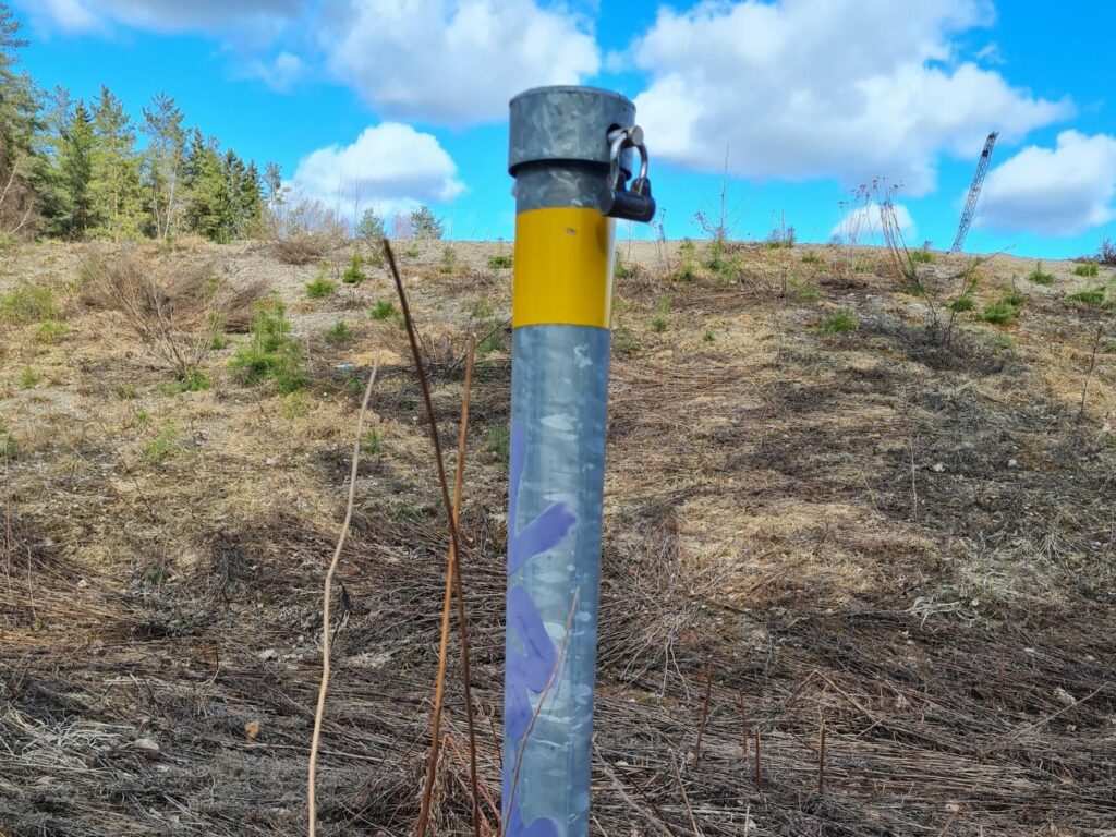 Metallinen maahan upotetun putken pää törröttää suorana maastossa.