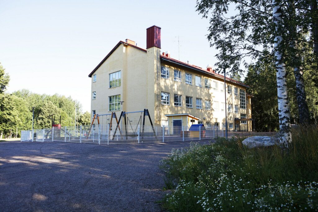 Vaaleankeltainen koulurakennus kesällä kuvattuna
