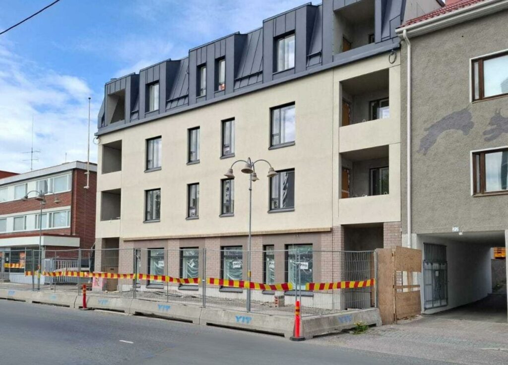 Hieno uusi 4-kerroksinen vaalea talo, jonka edustalla rakennustyömaa-aidat.