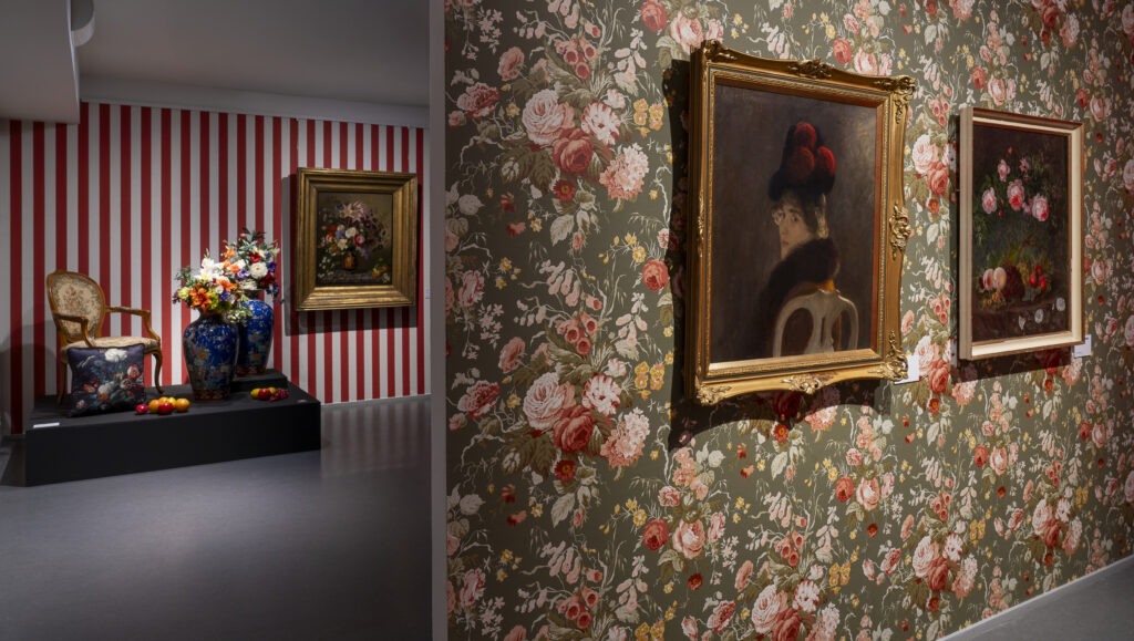 Taideteoksia ja esineistöä Riemu-museoiden näyttelysaleissa joiden seinät on tapetoitu kukkakuvioin.