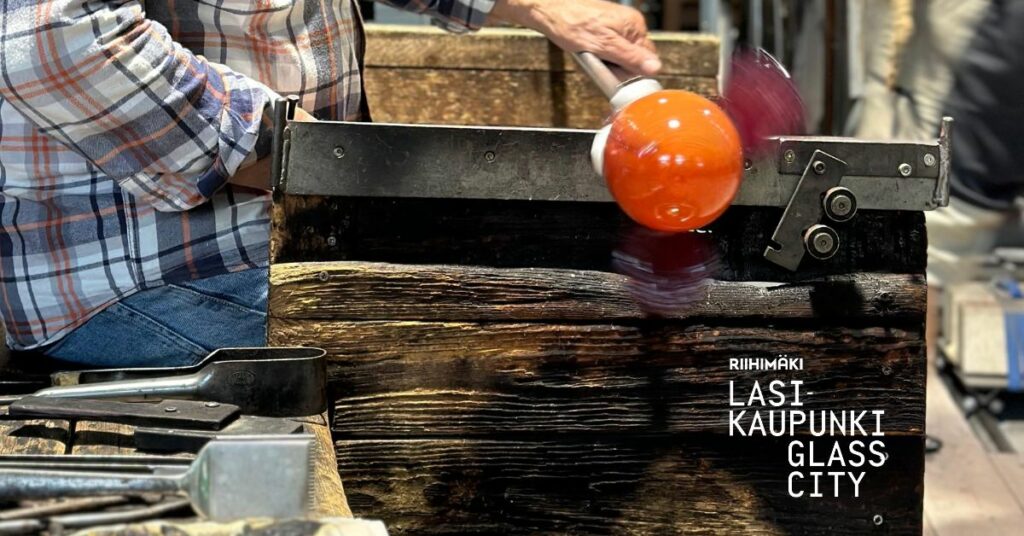 Miehen käsi pitää kiinni lasipilliä, jonka päässä oranssi lasipallo