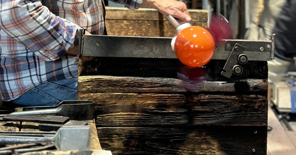 Miehen käsi pitää kiinni lasipilliä, jonka päässä oranssi lasipallo