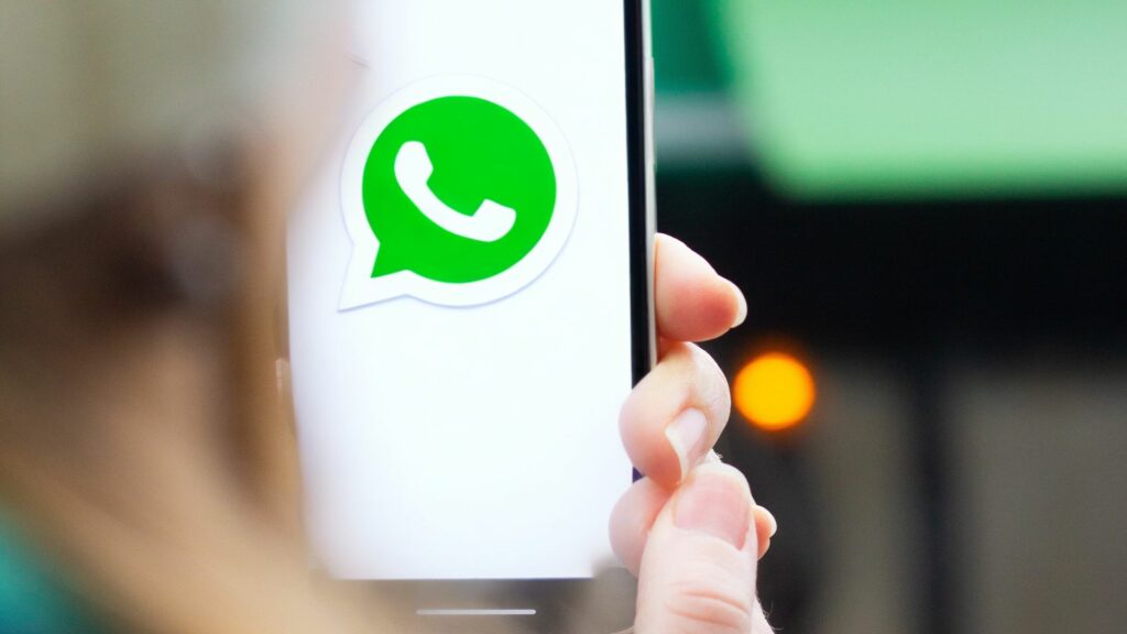 kädessä puhelin, jonka näytöllä whatsapp-logo.