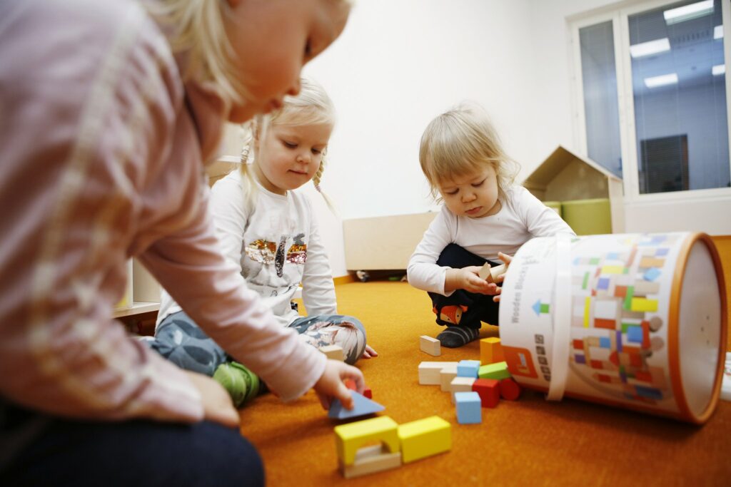Kolme lasta leikkimässä palikoilla päiväkodin lattialla.