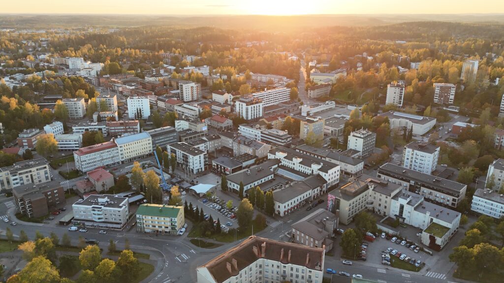 Viistoilmakuva Riihimäen keskustasta. Aurinko näkyy horisontissa.