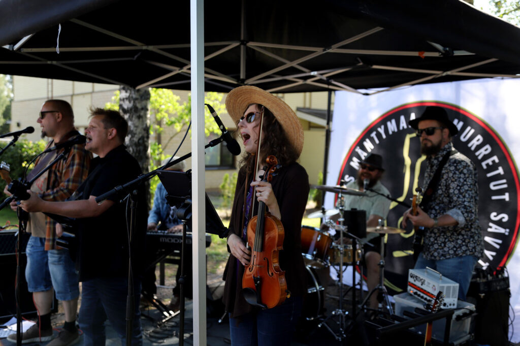 Kolmihenkinen bändi soittamassa lavalla katoksen alla.