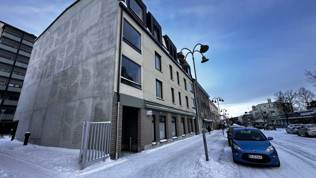 Lumisen kaupunkikeskustan maisemassa uusi kolmikerroksinen kerrostalo.