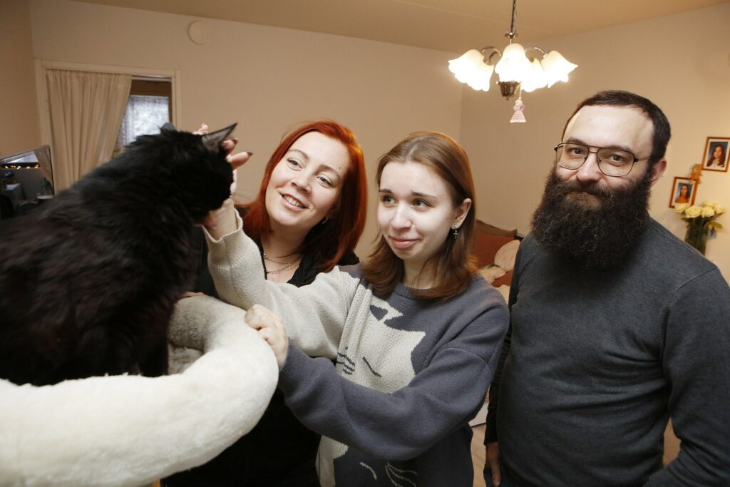 Kolmehenkinen perhe ihastelemassa kissaa sisällä kotona.