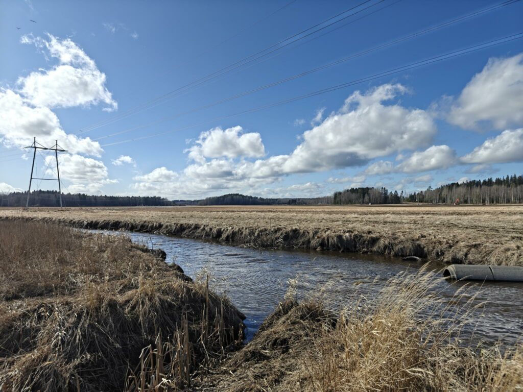Edustalla Vantaanjoki, jonka takana avoin peltoalue. Kuvassa näkyy voimajohtolinja.