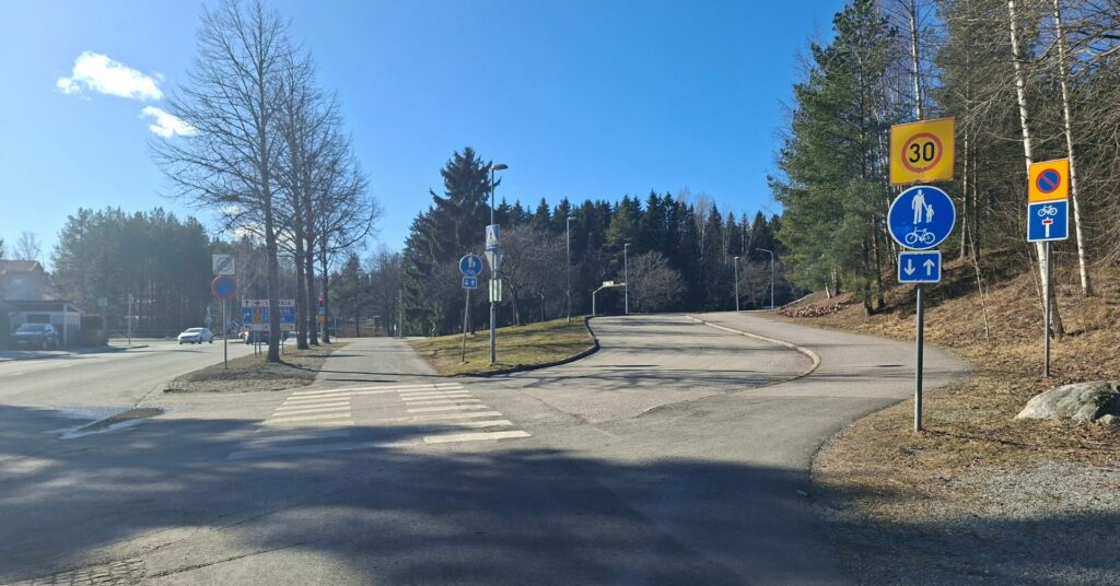 Alkukeväistä taajamamaisemaa, jossa asfaltoitua ajoväylää ja kevyen liikenteen väylää.