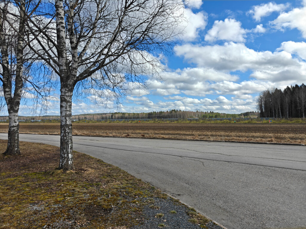 Edustalla asfaltoitu tie, jonka takana avoin peltoalue. Peltoalueella näkyy aurinkopaneeleja.