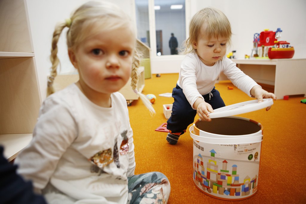 Vakavailmeinen tyttö päiväkodin lattialla leikkimässä toisen pikkulapsen kanssa.