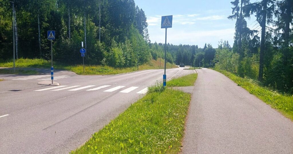 kuva tiestä, joka kulkee metsän siimeksessä ja kaukana näkyy auton hahmo. Kuvan edustalla on suojatie ja kevyenliikenteen väylä