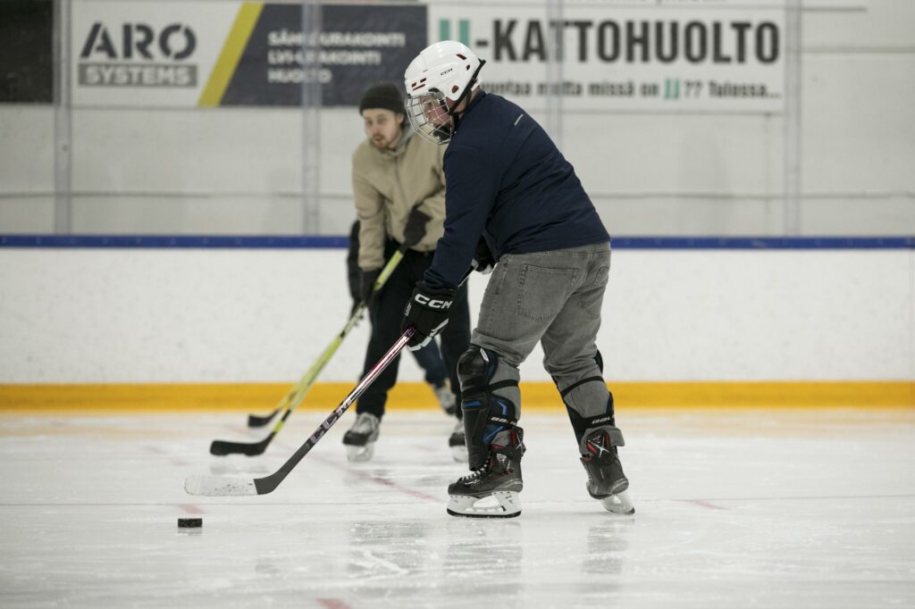 Kaksi nuorta pelaamassa jääkiekkoa sisähallissa.