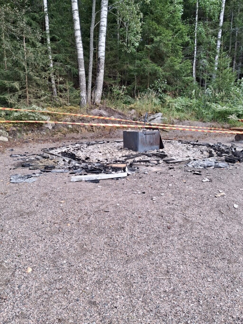 Hiekalla musta hiiliympyrä, keskellä metallinen laatikko.