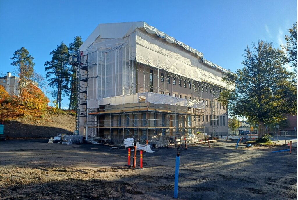 Kolmekerroksinen vaalea remontoitava rakennus.