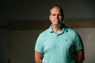 Vaaleanvihreään pikeepaitaan pukeutunut mies, tumma tausta.