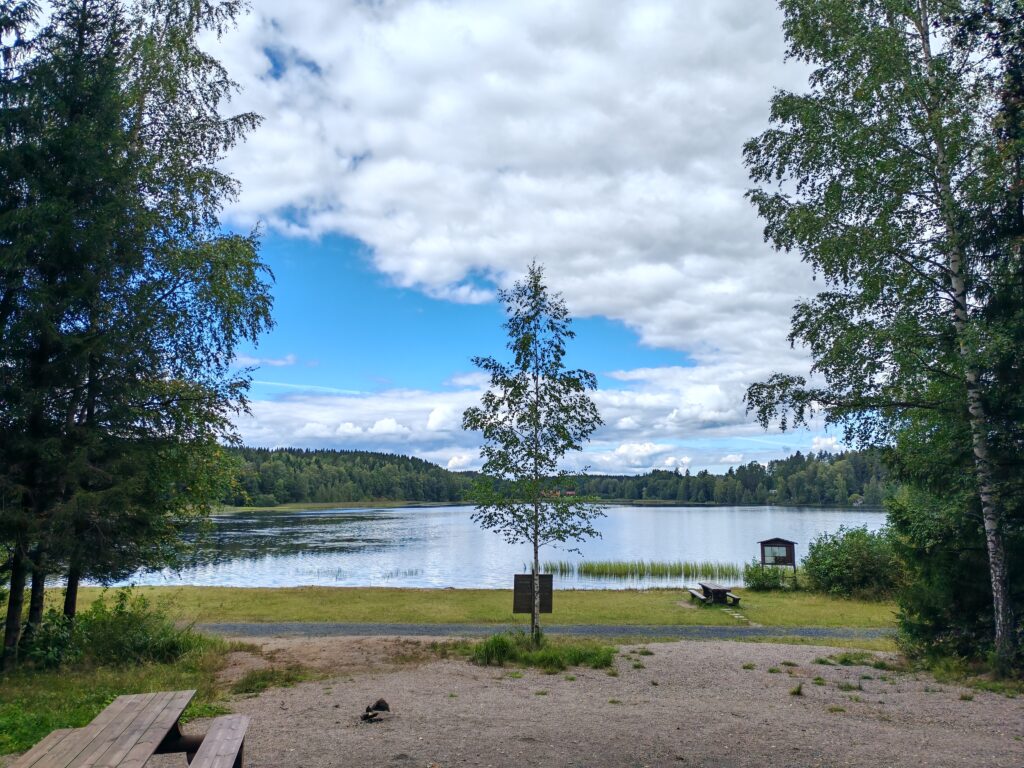 Järvimaisema. Etualalla piknikpöytä ja hiekkaranta.