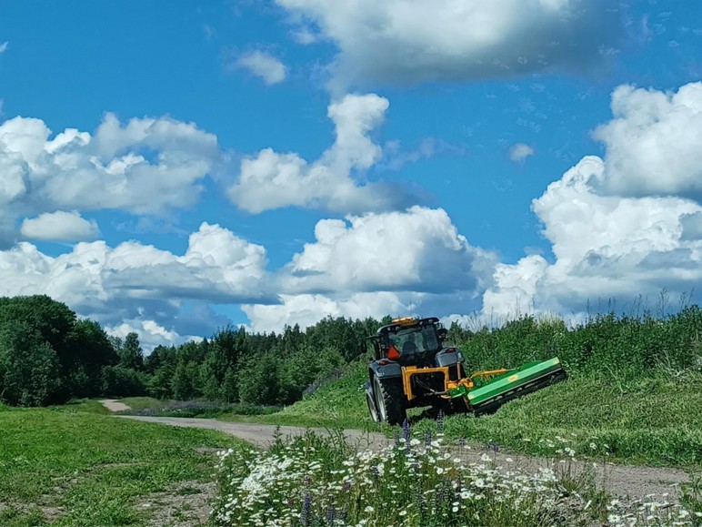 Niittokone niittää hiekkatien vehreää pengertä.